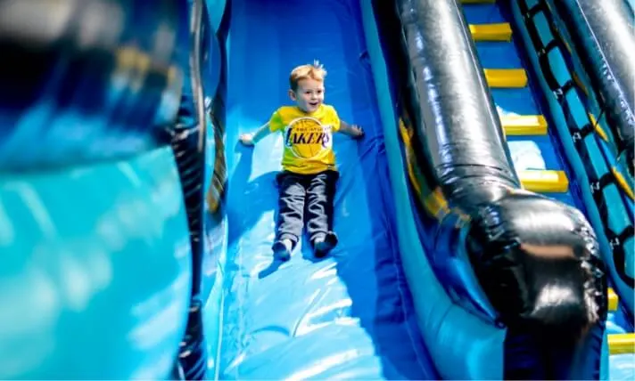 Young child sliding down a large blue inflatable slide at an indoor play centre.