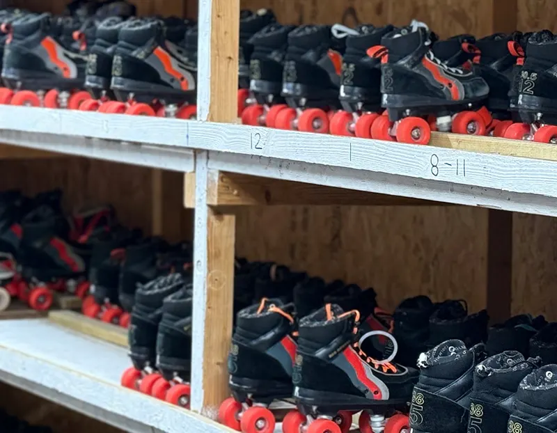 Shelves displaying black roller skates with red wheels, organised by size.