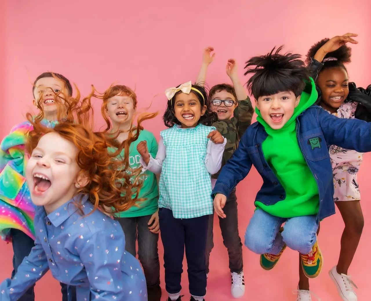 Group of children jumping and laughing together against a pink background.