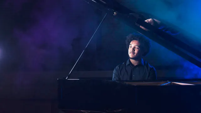 Pianist performs at a grand piano under blue stage lighting.