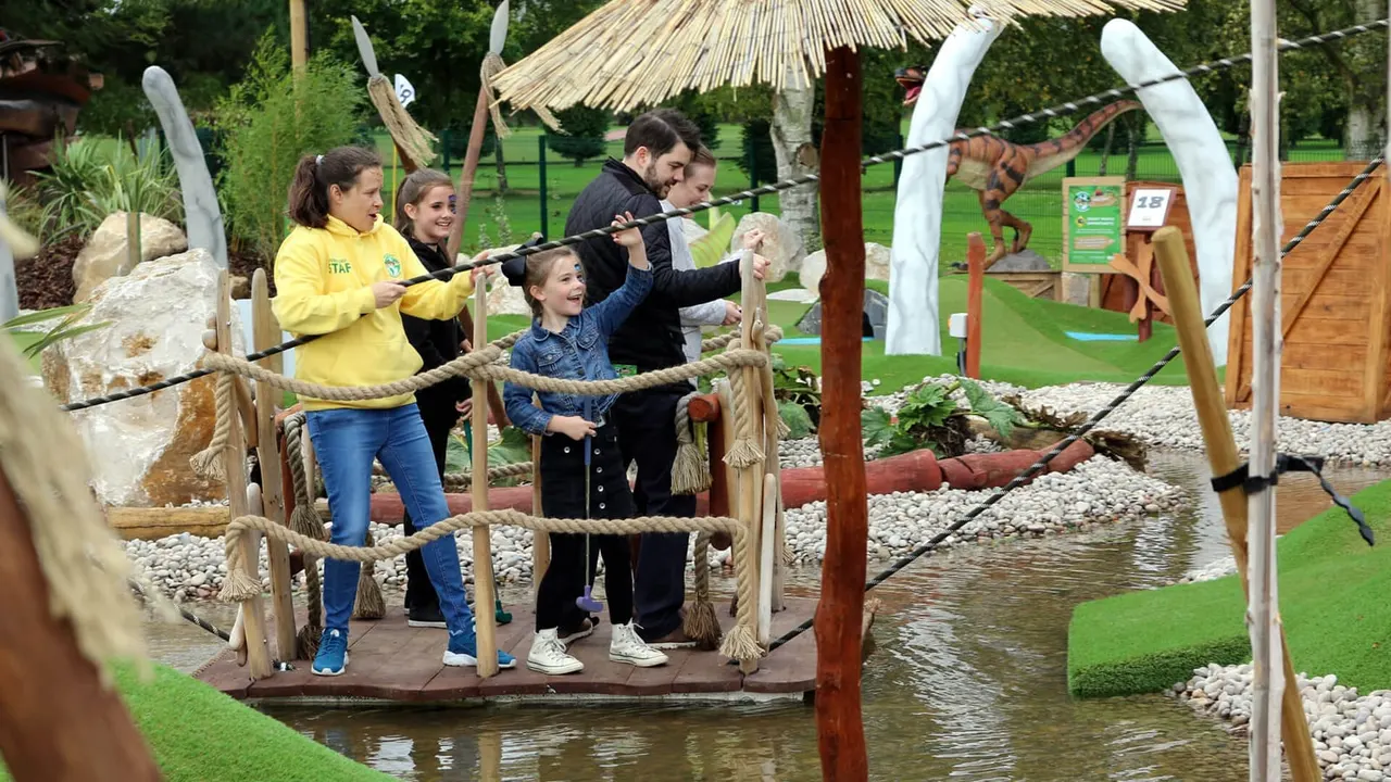 Family on wooden raft hole 18 with staff and dinosaur props at Lost World CrazyPutt