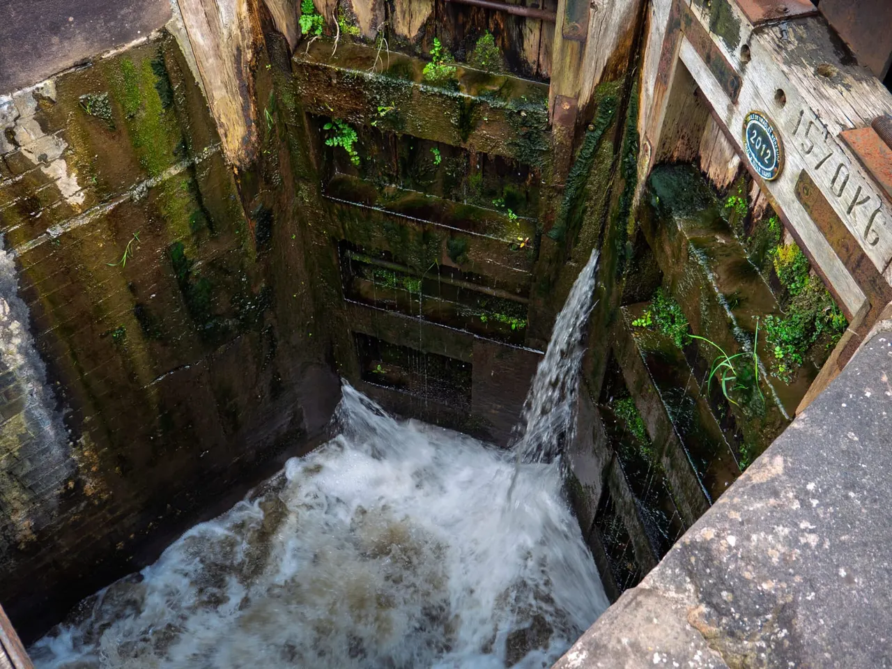 Water cascades down through a moss-covered lock with wooden gates and metal railings.