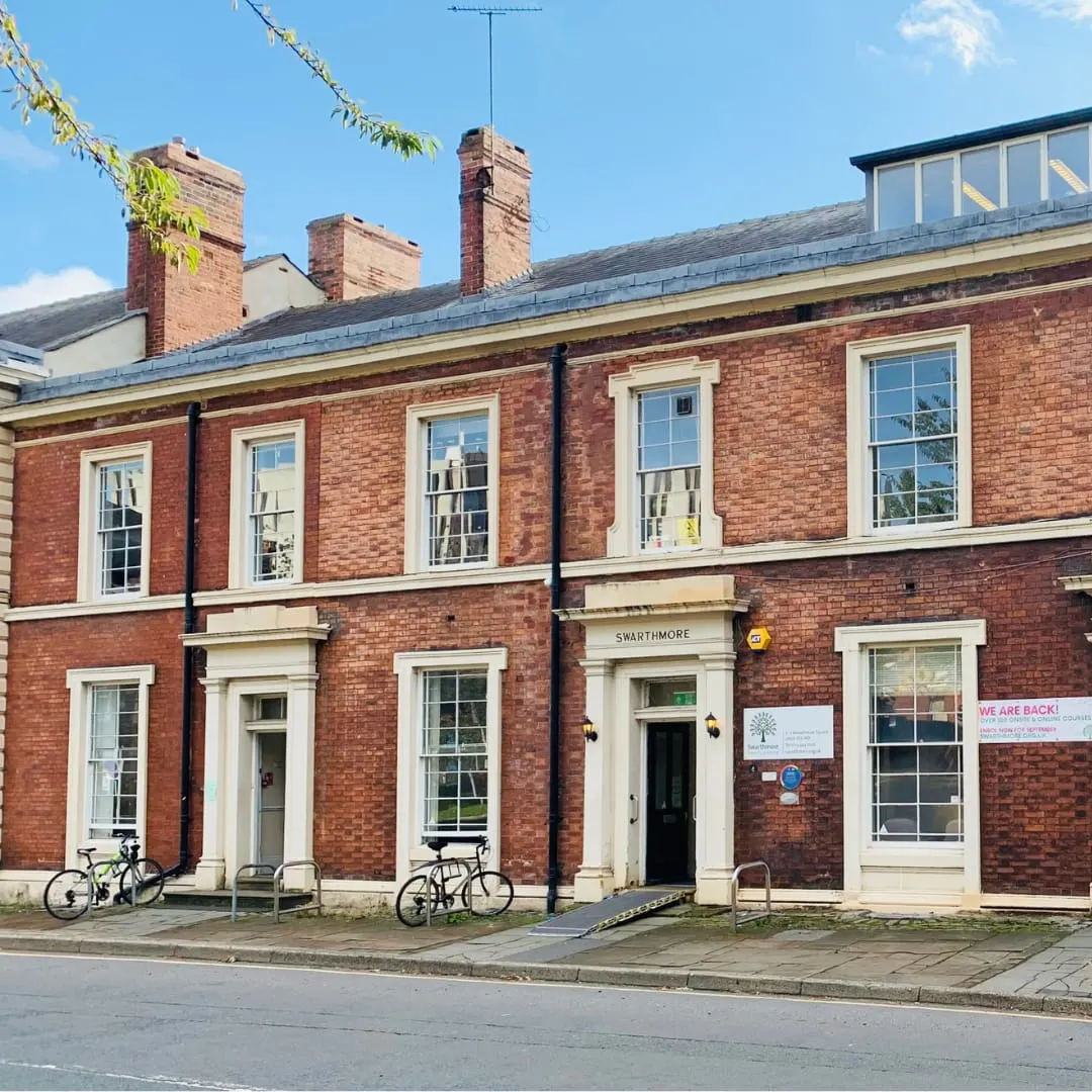 Victorian red brick building with cream-coloured window frames and multiple chimneys, bicycles parked outside.