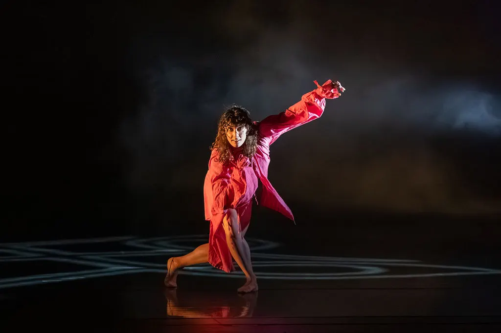 Dancer in red costume performing on stage with dramatic lighting and flowing fabric.