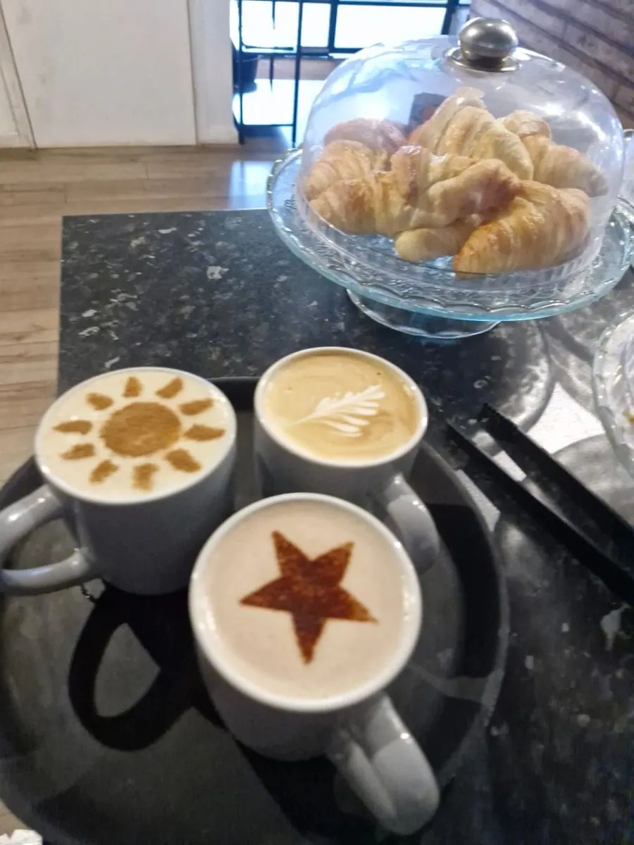 Three white mugs of coffee with latte art designs and croissants under a glass dome on a dark counter.
