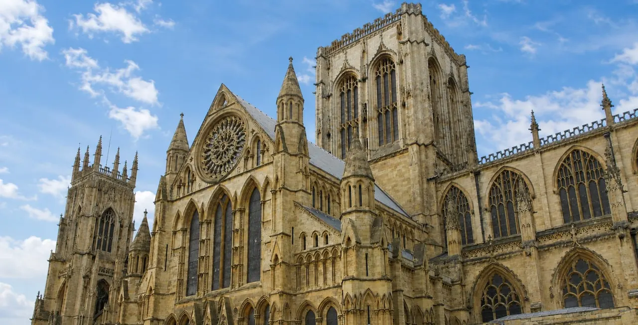 Gothic cathedral with stone towers, ornate windows and spires against a blue cloudy sky.