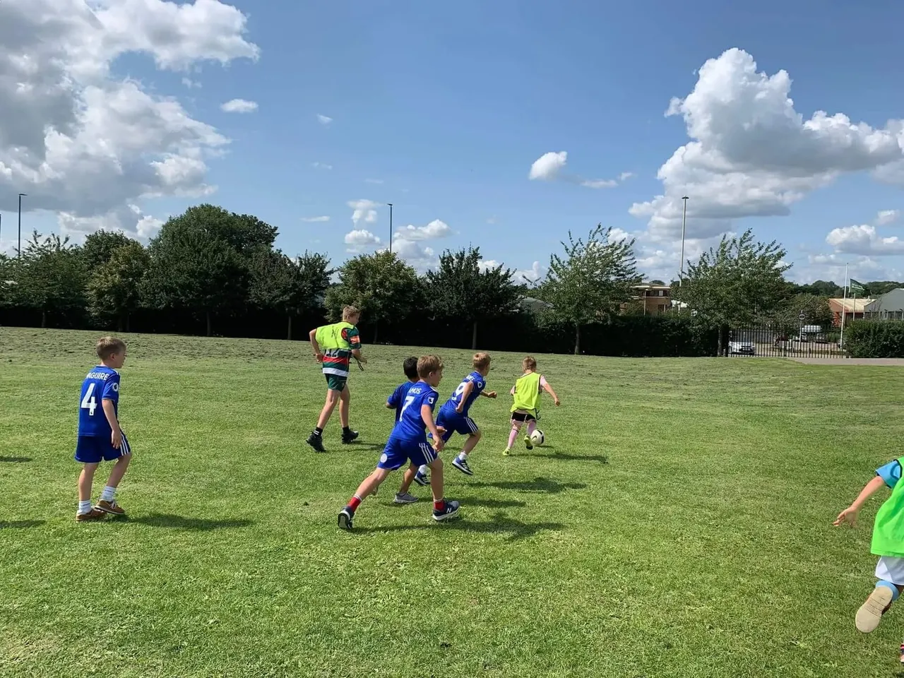 Children playing football on a grass pitch during a sunny day at an outdoor sports facility.