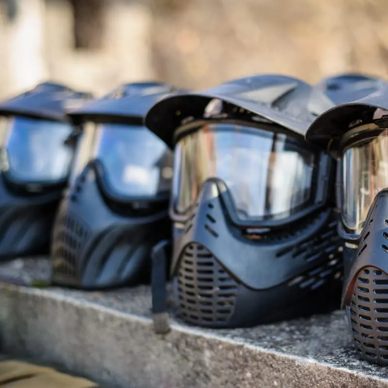 Row of blue and black paintball masks with protective visors lined up on a concrete ledge.