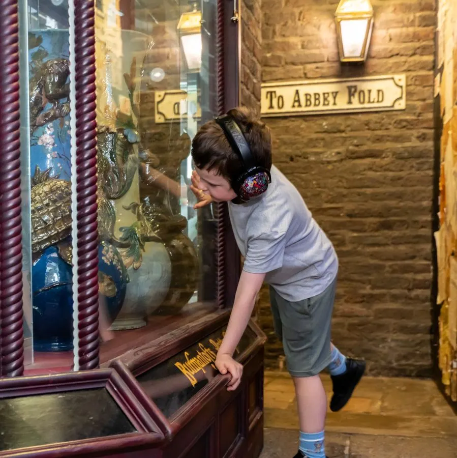 Young child wearing headphones interacting with a display case in a stone-walled museum corridor.