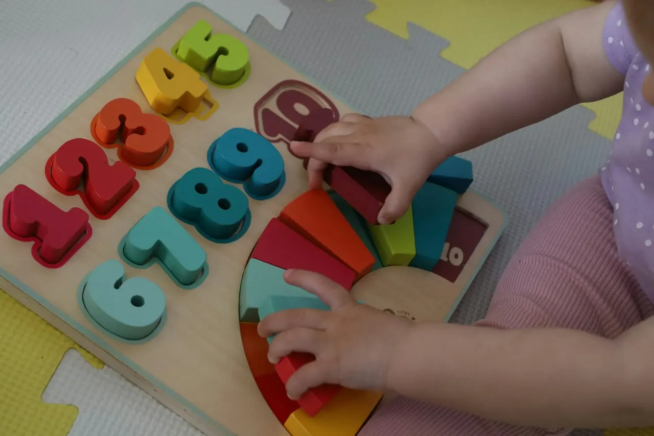 Young child playing with a wooden number and shape sorting puzzle toy.