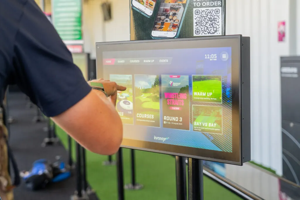 Person in dark sleeve touching interactive digital menu screen displaying golf course options and events.