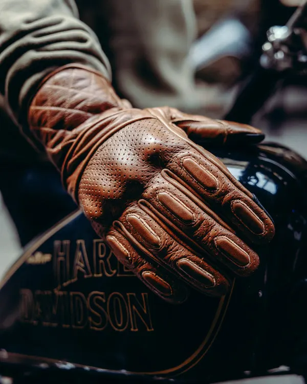 Close-up of brown leather motorcycle gloves worn by a rider's hand resting on a bike tank.