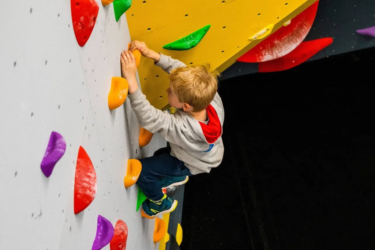 Young child climbing an indoor rock wall with coloured handholds.