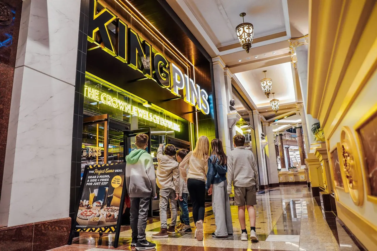 Group of visitors queuing outside a brightly lit fast food restaurant with yellow and black signage in an indoor shopping mall.