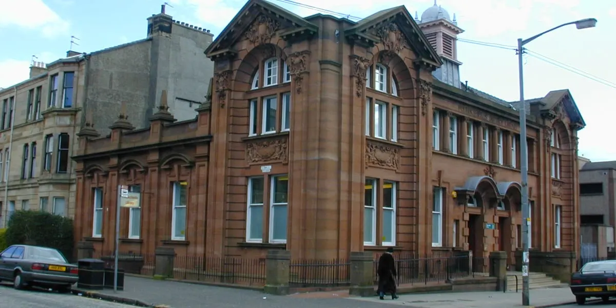 Victorian sandstone library building with ornate architectural details and arched windows on a street.