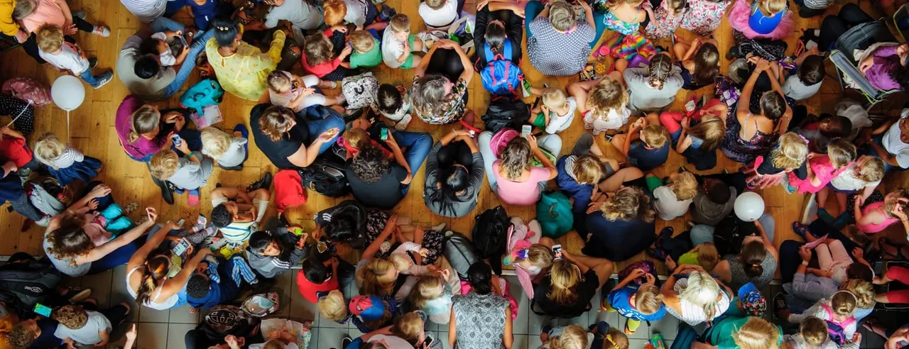 Overhead view of a large group of children and adults dancing and socialising on a wooden floor at an indoor event.
