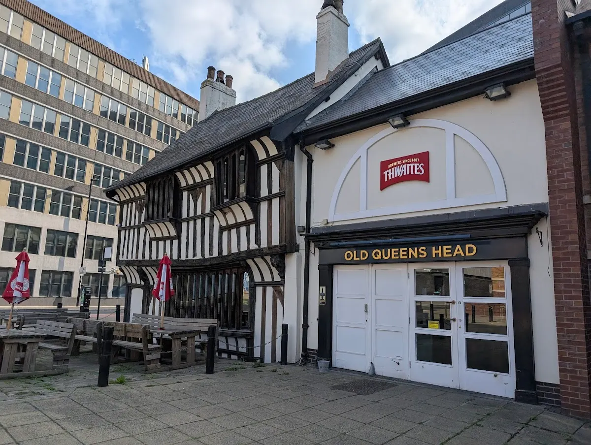 Historic black-and-white timber-framed pub building with outdoor seating area and modern office buildings behind.