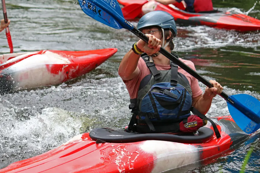 Person whitewater kayaking in red kayak wearing helmet and life jacket on river.