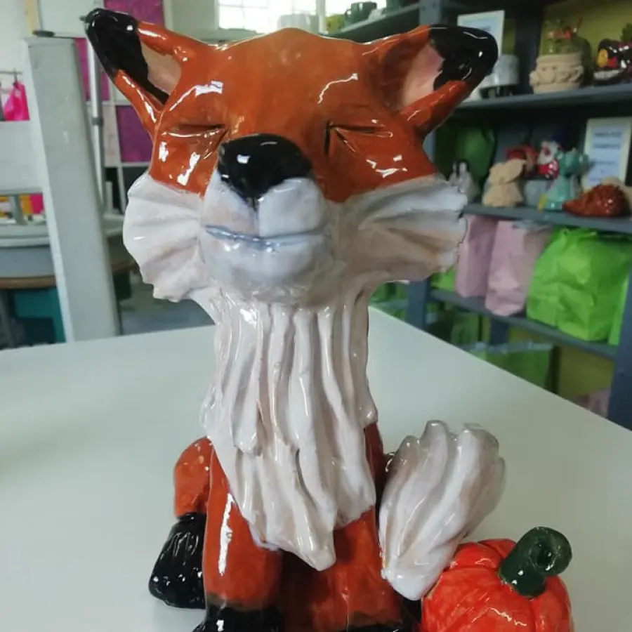 Glossy ceramic fox figurine with orange, white and black colouring displayed on a table indoors.