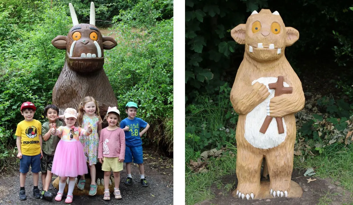 Children posing with wooden character sculptures among green foliage at a country park.