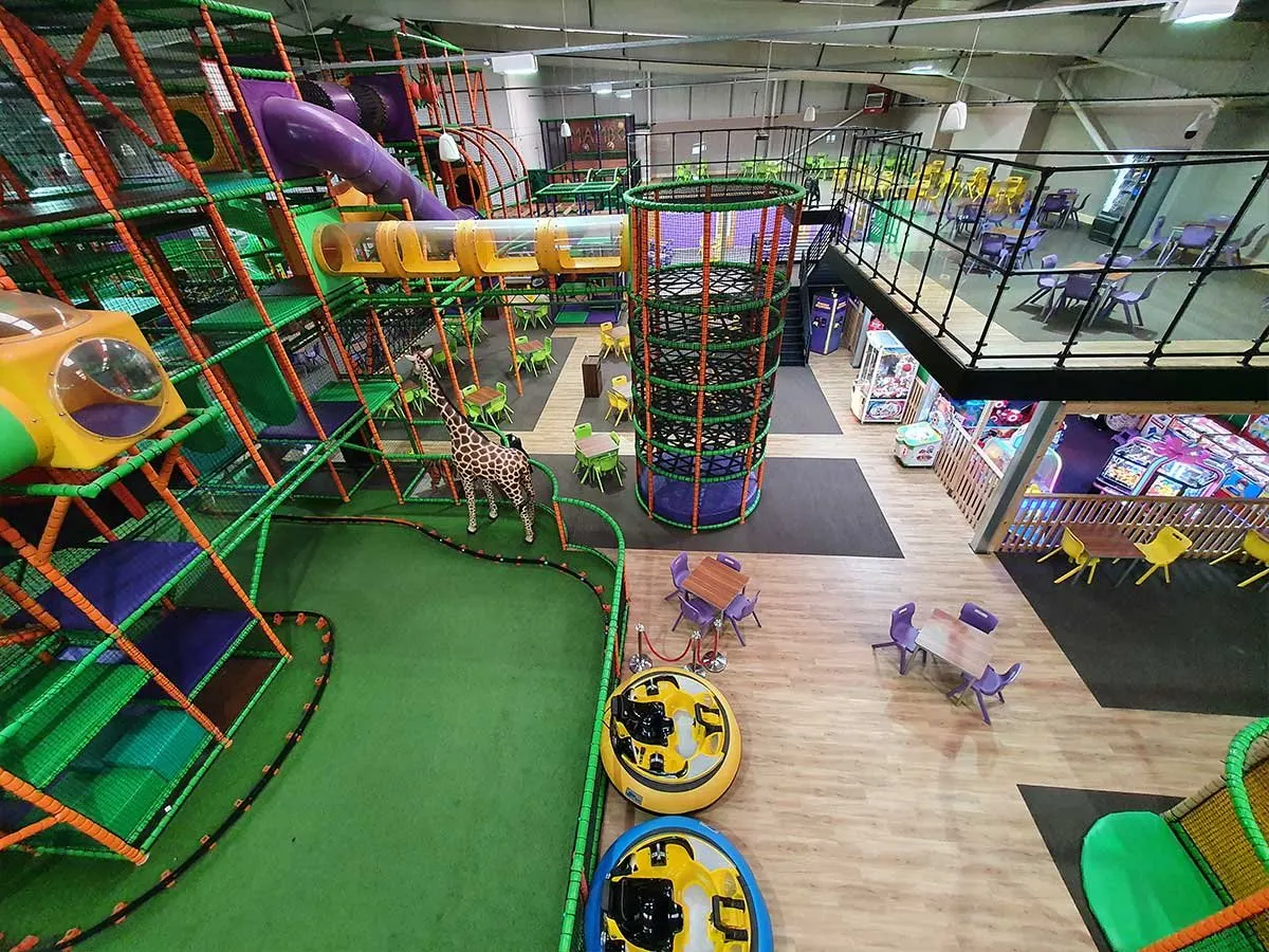 Indoor play centre with colourful climbing structures, slides, and activity equipment surrounding an open floor area with seating.