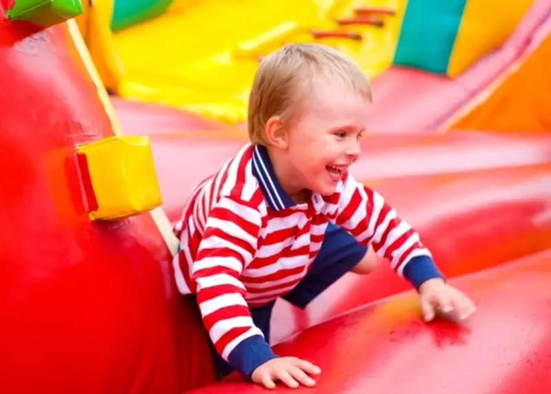 Young child laughing whilst climbing on colourful inflatable play equipment.