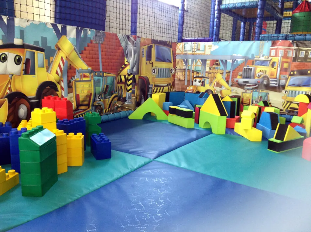 Indoor soft play area with construction vehicle theme, featuring foam blocks, tunnels and padded play structures.