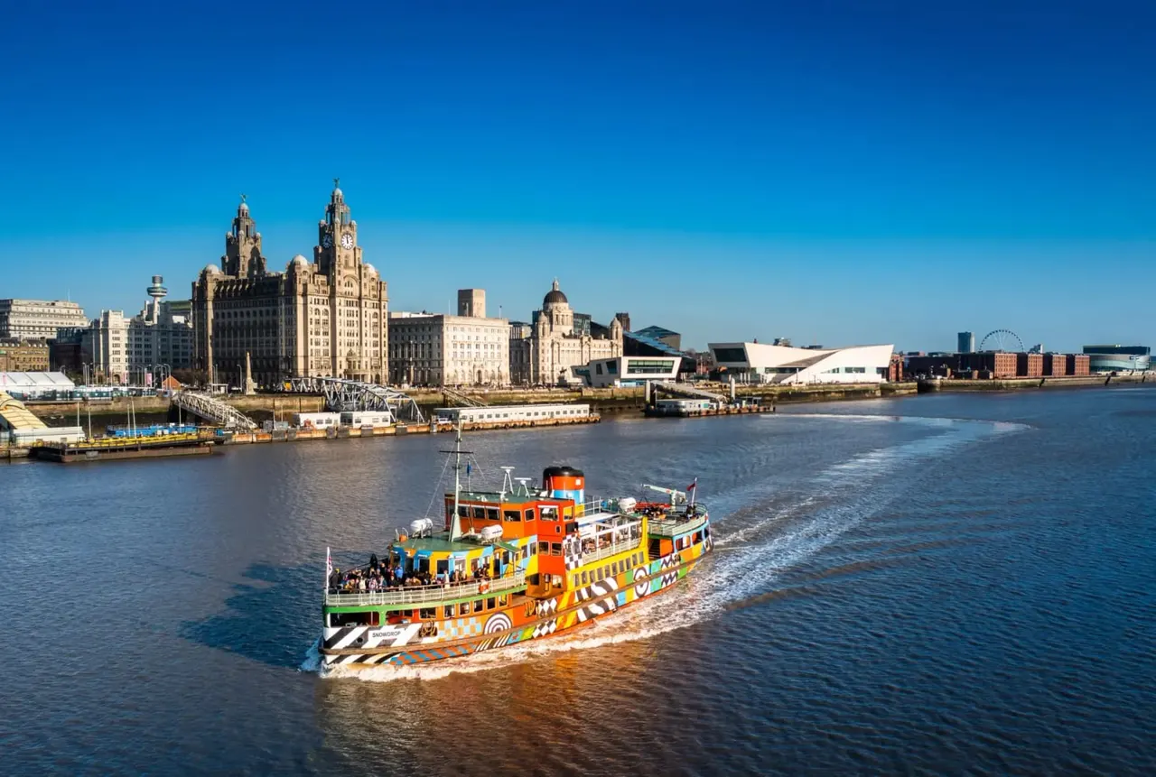 Colourful passenger ferry boat on the River Mersey with Liverpool waterfront and historic buildings in the background.