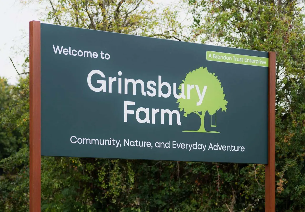 Welcome signboard for Grimsbury Farm set against green woodland in the background.