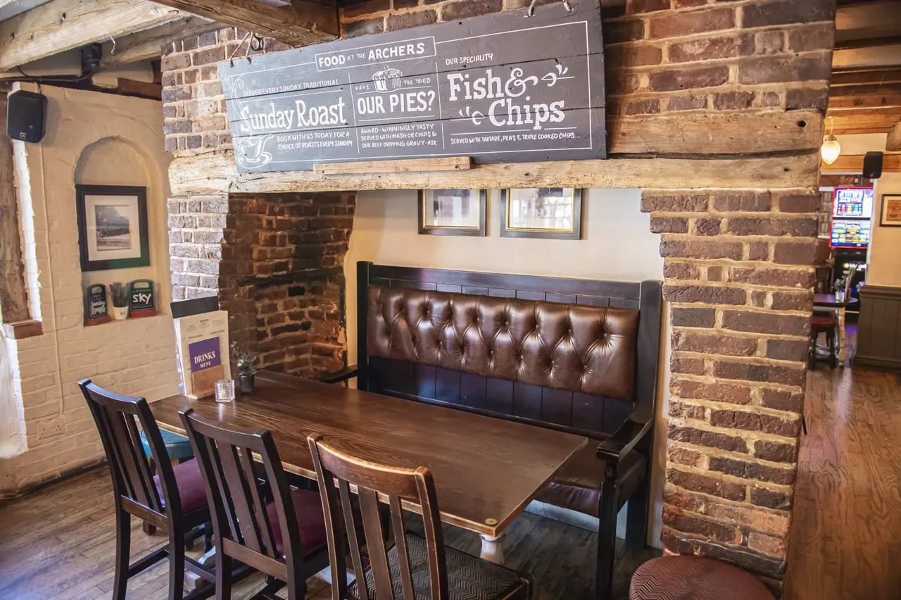 Dining booth with wooden table and brown leather seating in a pub with exposed brick walls and menu board advertising Sunday roast and fish and chips.