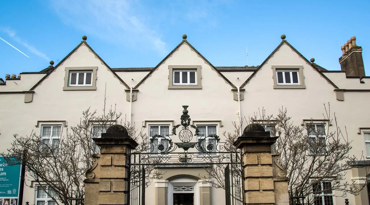 Facade of a cream-coloured Georgian townhouse with symmetrical gabled roofs, ornate iron gates, and bare winter shrubs.