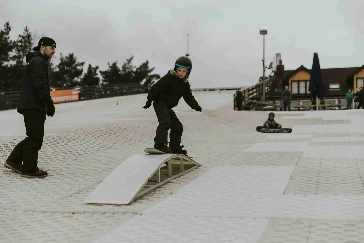 A person in a blue helmet skateboarding over a ramp at an outdoor skate park with onlookers watching.