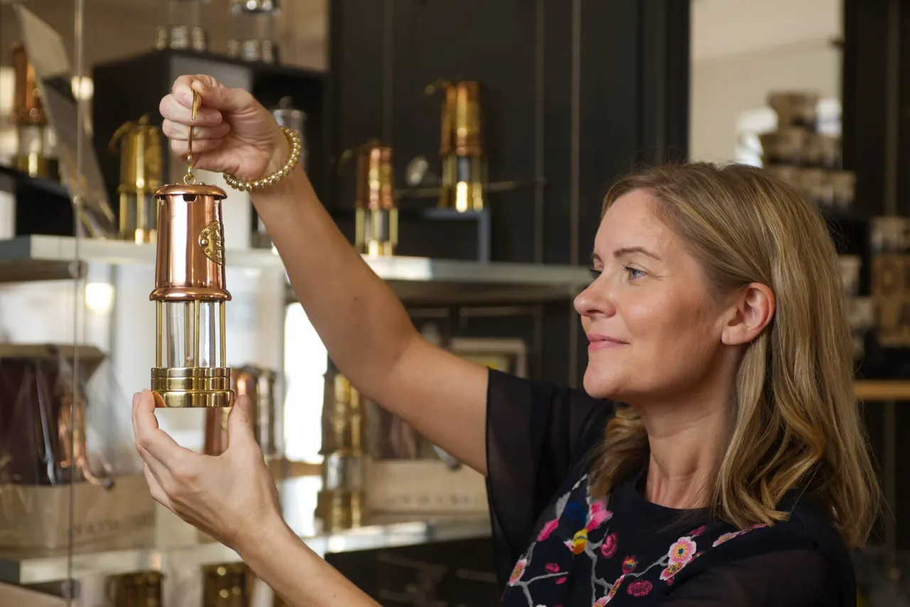 Woman examining a copper and brass miners' lamp on display in a museum gallery.