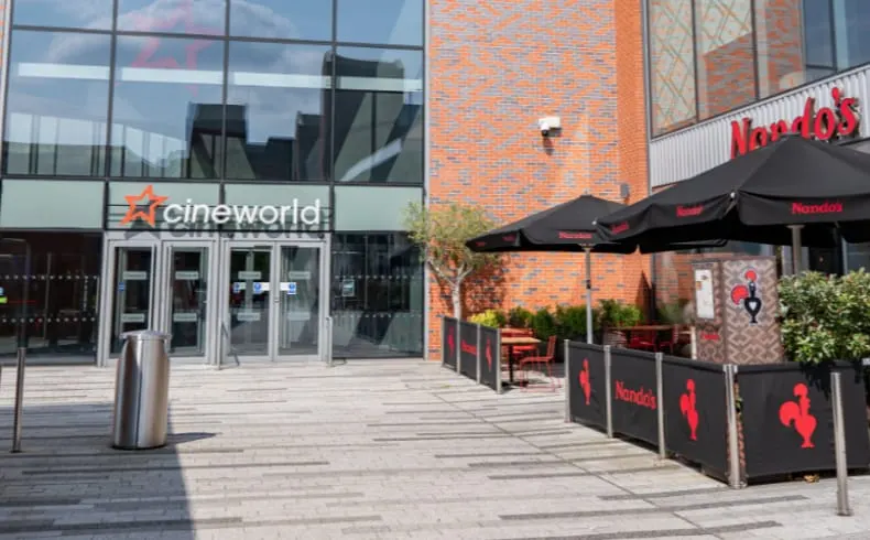 Exterior courtyard with Cineworld cinema entrance, black umbrellas, and Nandos restaurant seating area on brick buildings.