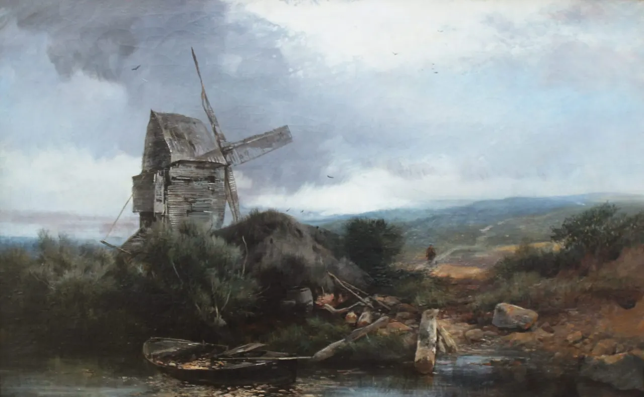 A weathered wooden windmill stands in a rural landscape with overgrown vegetation, a small boat, and distant hills under cloudy skies.