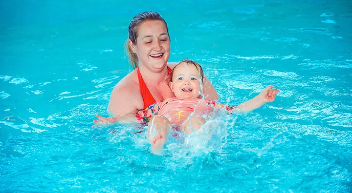 Adult and young child in swimming pool with inflatable aid, both smiling.