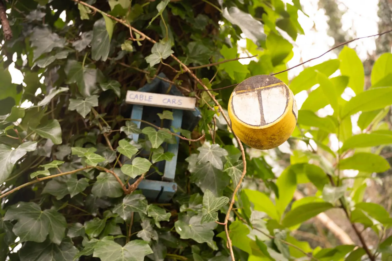 Yellow circular sign hanging from climbing foliage, with an eagle cars sign partially visible behind the vines.