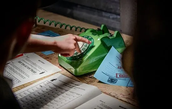 A person's hand reaching toward a green decorative telephone on a desk covered with paperwork and documents.