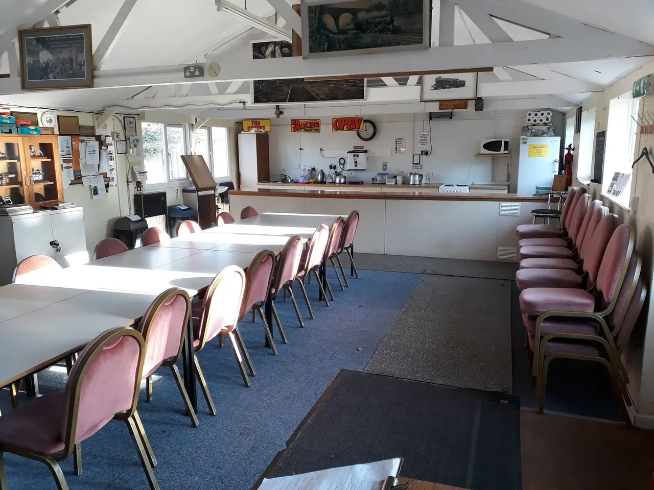 Interior of a heritage railway station café with tables, burgundy chairs, service counter and vintage railway memorabilia on walls.