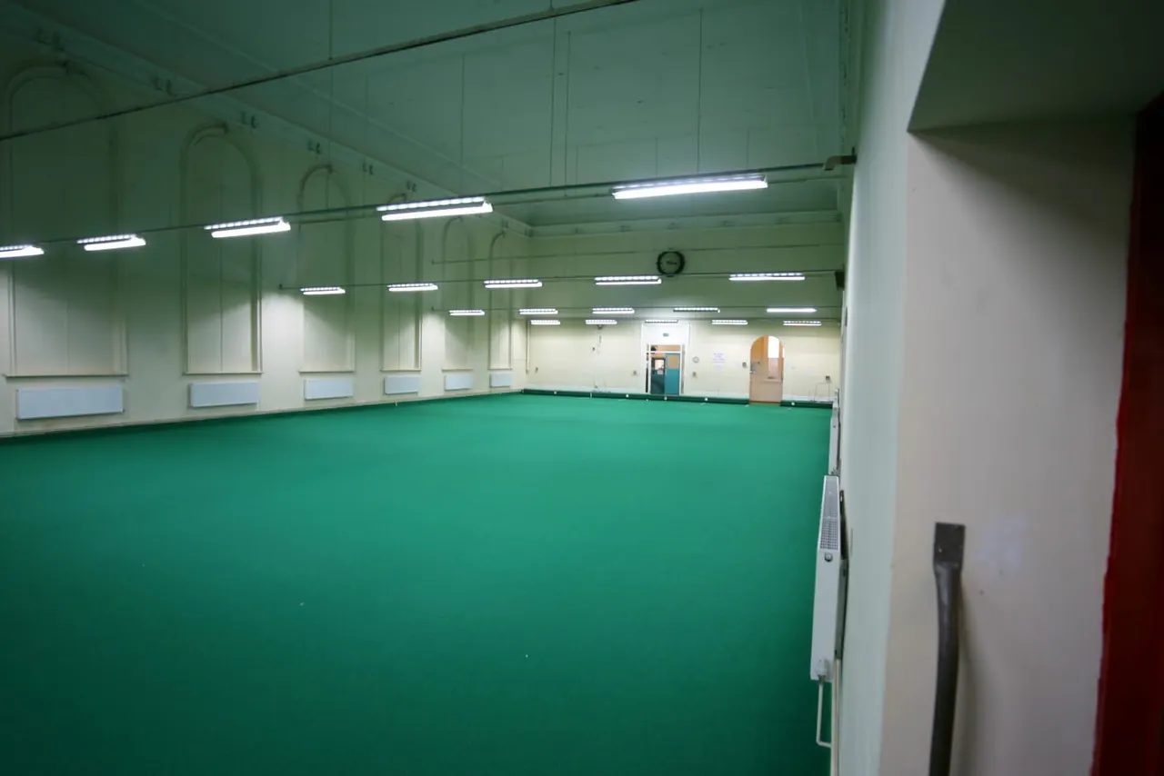 Empty indoor bowls green with fluorescent lighting and cream-coloured walls.