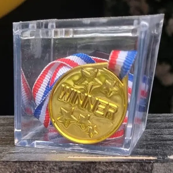 Gold medal with red, white and blue ribbon in clear plastic case on wooden surface.