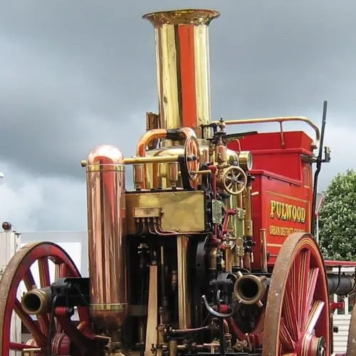 A vintage brass and red steam-powered traction engine with large spoked wheels parked outdoors.