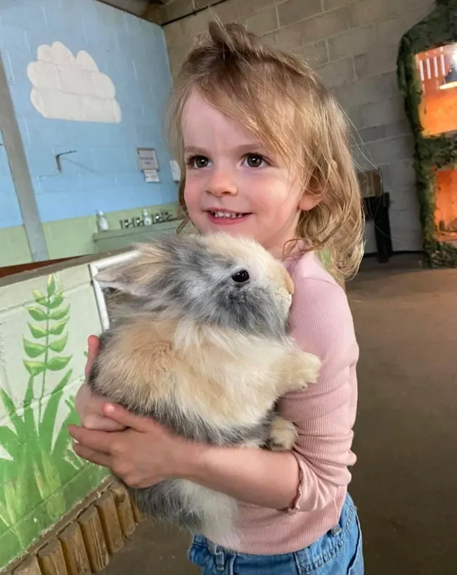 Young child holding and smiling at a fluffy guinea pig indoors.