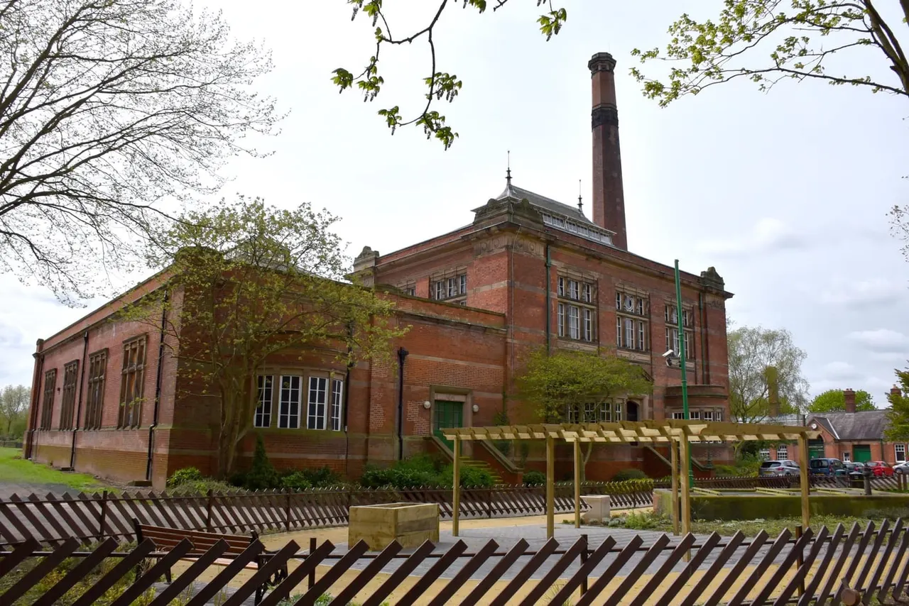 Historic red-brick Victorian pumping station with tall chimney, surrounded by trees and wooden fencing.