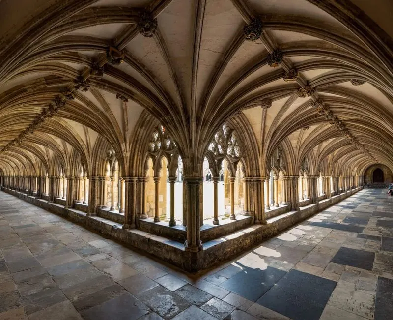 A symmetrical medieval stone cloister with vaulted Gothic arches, columns and tracery windows opening onto a central courtyard.