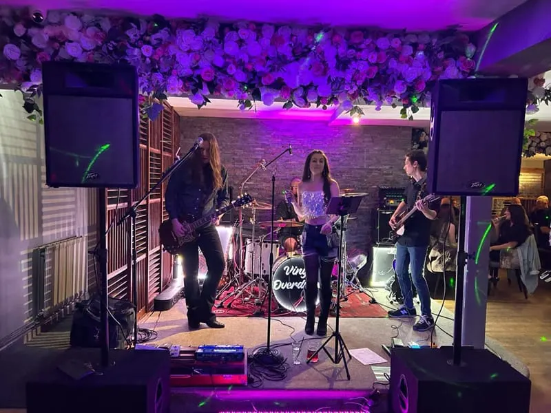 Band performing on stage with purple lighting and hanging floral decorations in a music venue.