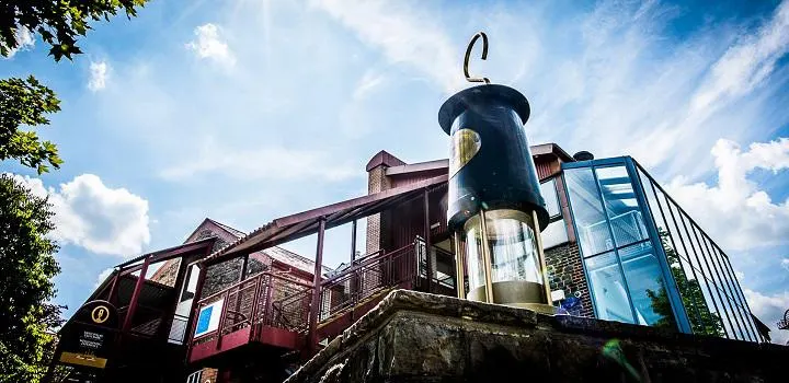 A large suspended mining pit cage and lantern displayed above a historic mining building against a blue sky.