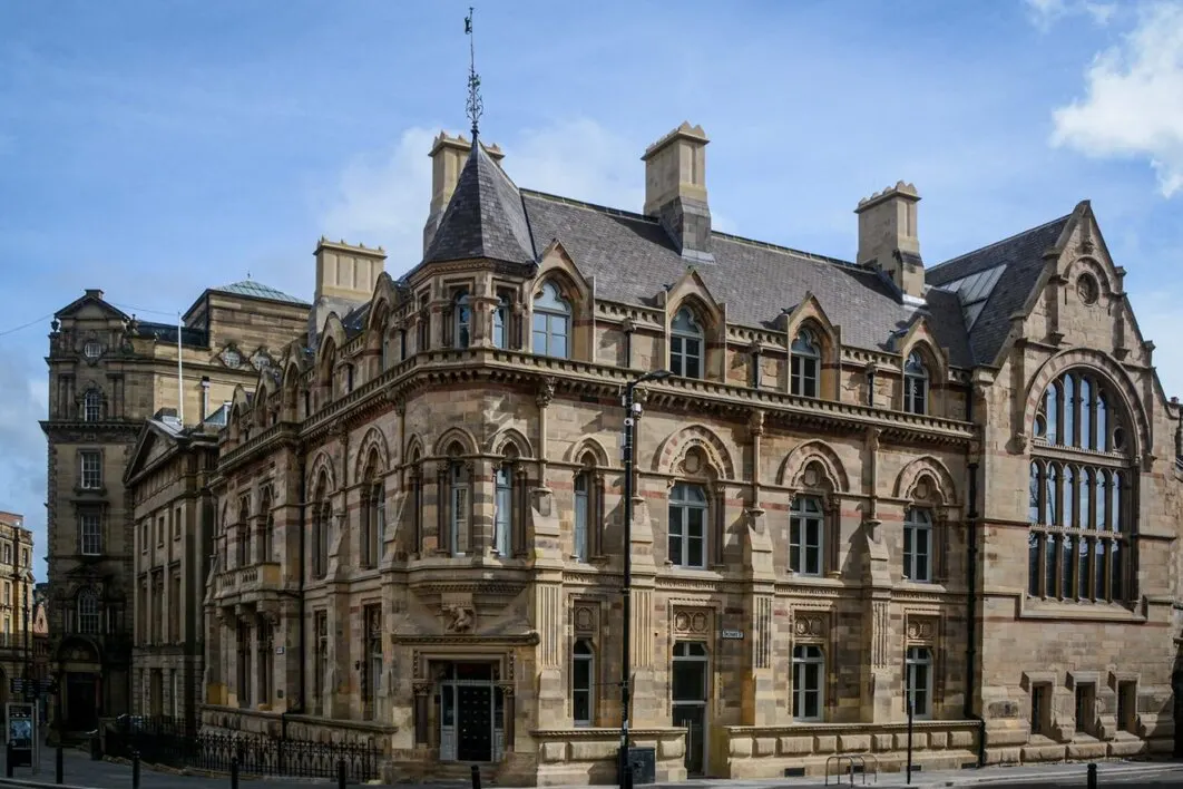 Grand Victorian stone building with ornate architecture, arched windows, turrets and decorative stonework under blue sky.