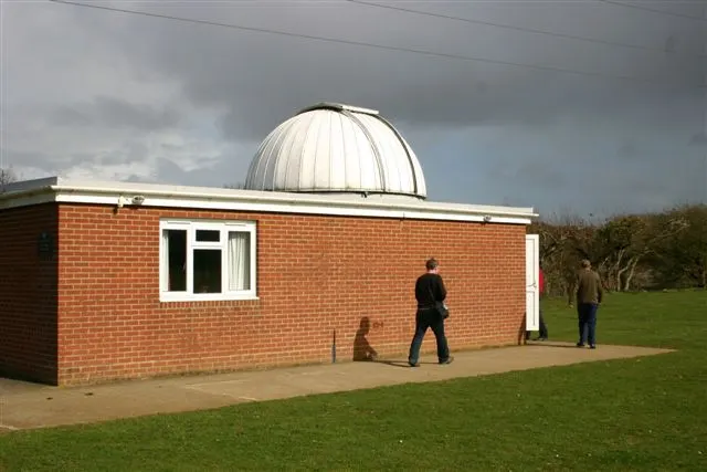 Visitors stand outside a brick observatory building with a white domed roof in a rural setting.