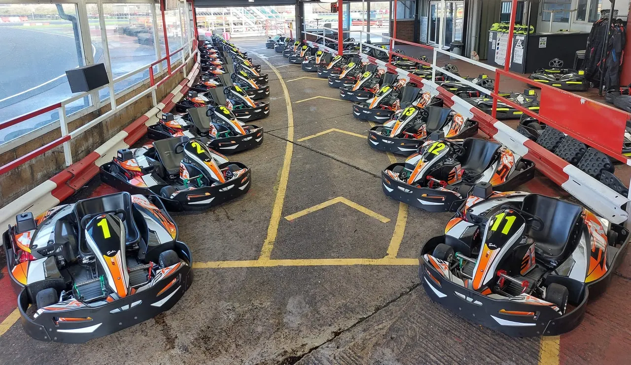 Rows of numbered go-karts parked in an indoor circuit garage with red barriers and yellow lane markings.